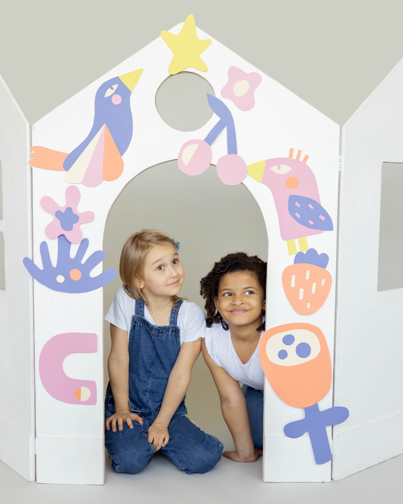 Two young girls posing in a makeshift paper gate decorated with paper art work its colourful.