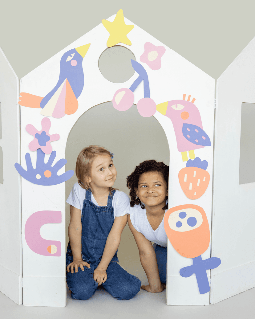 Two young girls posing in a makeshift paper gate decorated with paper art work.