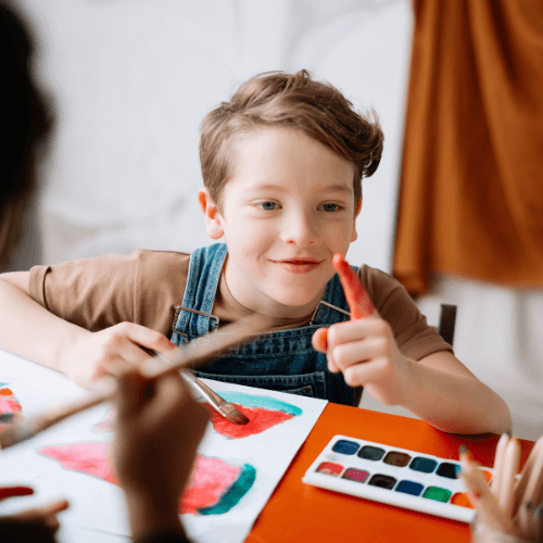 Little boy smiling holding up his finger with red paint on