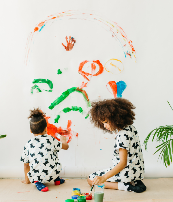 Two young children painting on a wall.